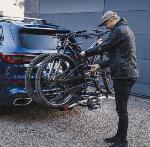 Thule EasyFold XT on back of SUV loaded with 2 bikes. Man is locking the bikes onto the rack