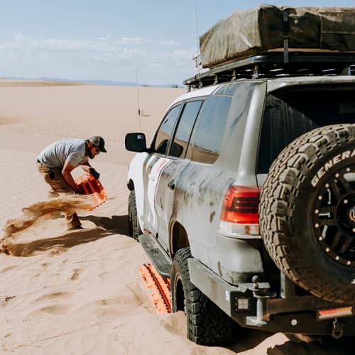 person using maxtrax recovery boards to get SUV with rack on it out of a sand ditch